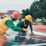 Dwaj instalatorzy paneli słonecznych na dachu w kaskach i uprzężach