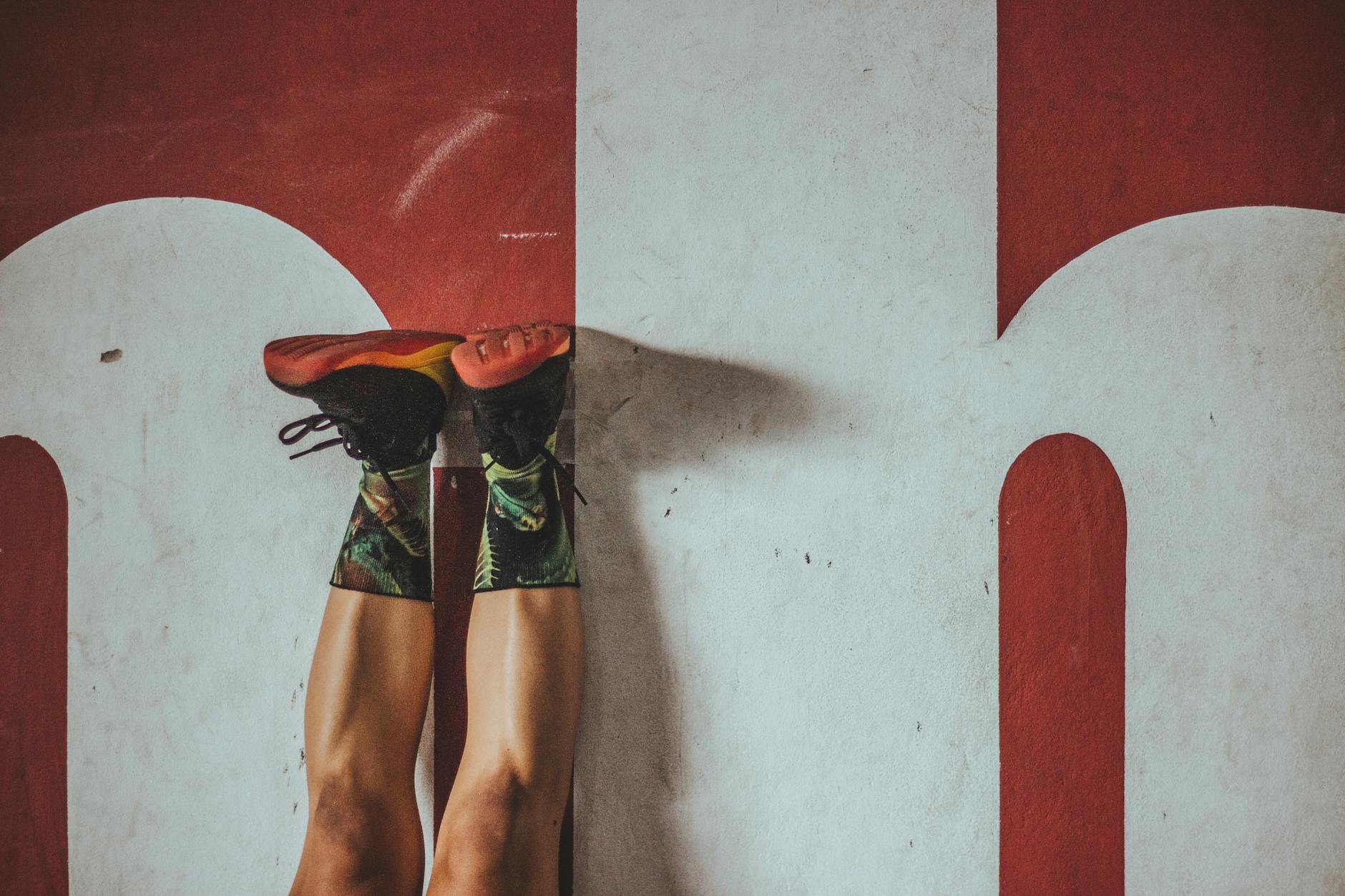 Osoba ćwicząca przy czerwonej ścianie w kolorowych skarpetkach i adidasach