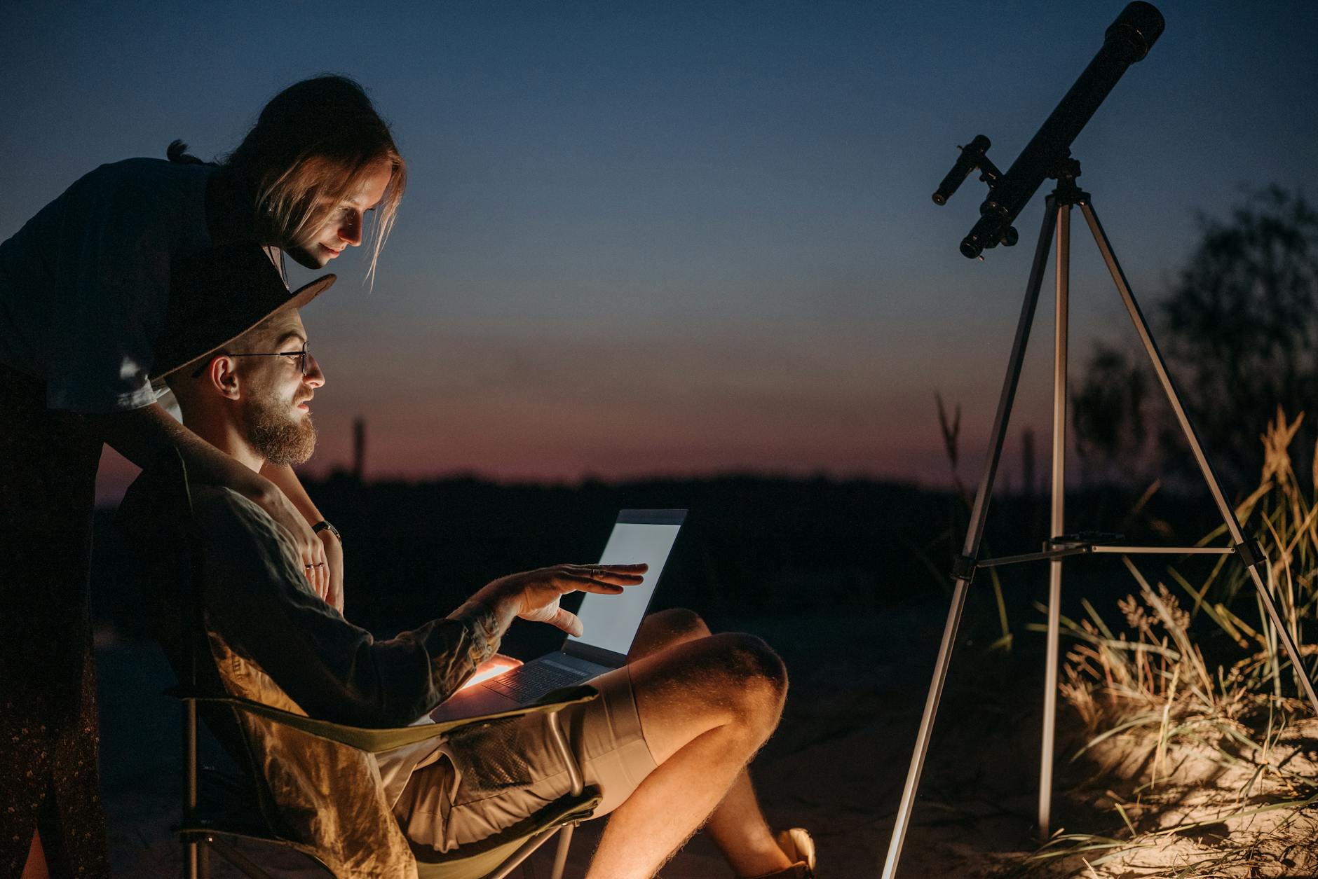 Pierwszy teleskop dla początkujących: jak wybrać mądrze Para ogląda nocne niebo przez teleskop, korzystając z laptopa na dworze