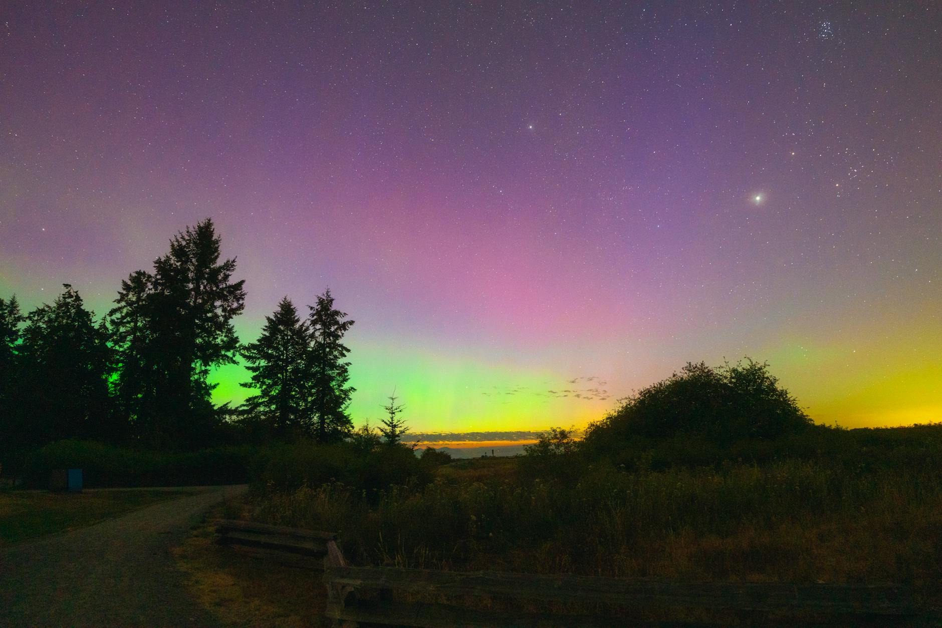 Zorza polarna nad spokojnym, wiejskim krajobrazem nocą