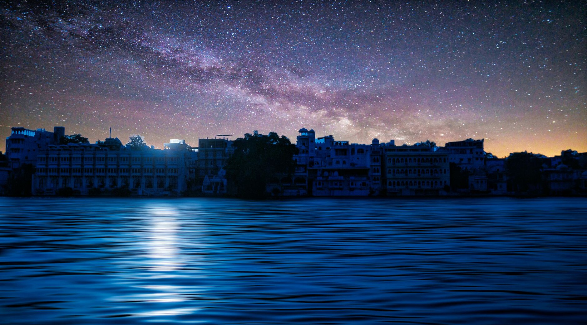 Jak zacząć astrofotografię w mieście i naprawdę widzieć więcej Droga Mleczna nad nocnym miastem odbijająca się w spokojnym jeziorze