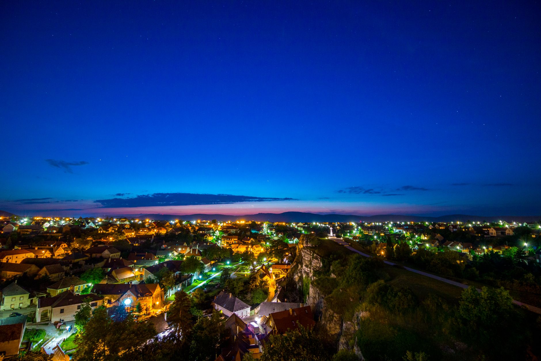 Między miastem a wsią: gdzie jest złoty środek dla udanych nocnych obserwacji nieba Małe miasteczko nocą sfotografowane z góry, otoczone wieczornym niebem