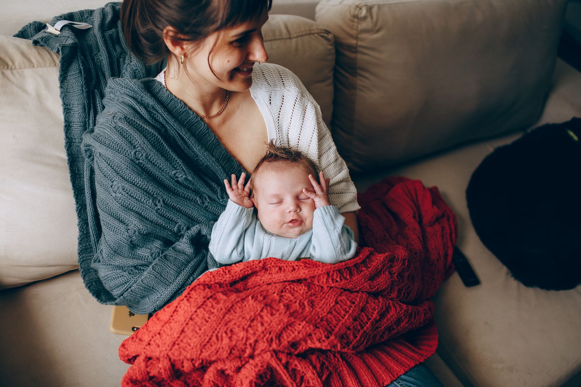 Mama trzyma śpiące niemowlę otulone kocem w domowym zaciszu