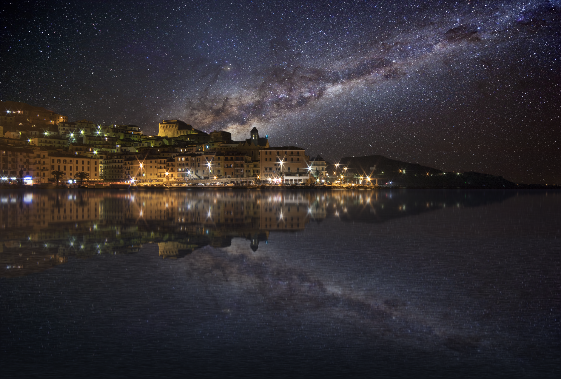 Nocna panorama miasta nad wodą z wyraźną Drogą Mleczną na niebie