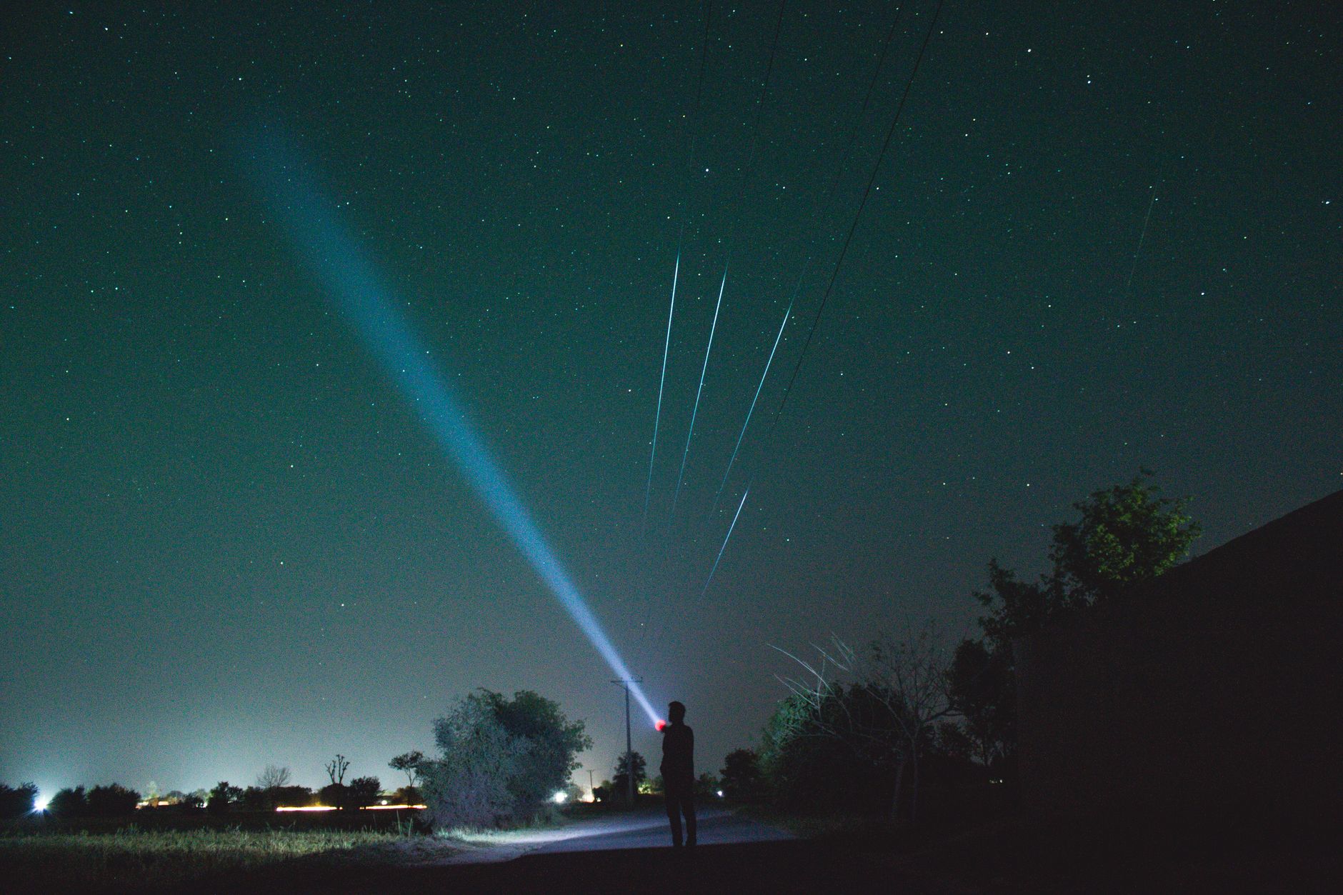Sylwetka osoby z latarką skierowaną w rozgwieżdżone nocne niebo
